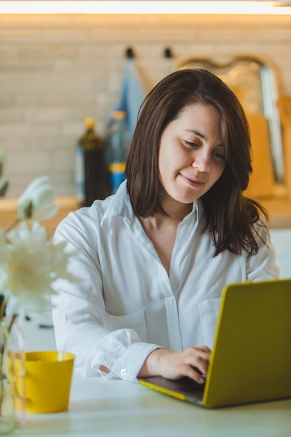 Young pretty caucasian woman talking on the phone sitting in front of laptop in the kitchen