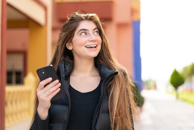 笑顔で外で携帯電話を使っている若い美しい白人女性