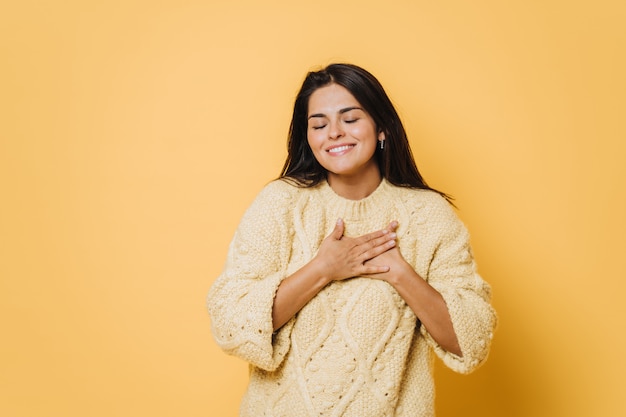 Young pretty caucasian woman wearing a yellow jumper, laughing keeping hands on heart, concept of happiness.