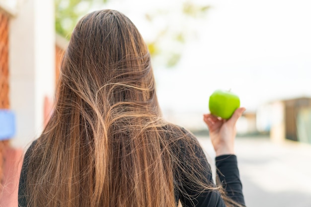 Молодая красивая белая женщина с яблоком на открытом воздухе в заднем положении