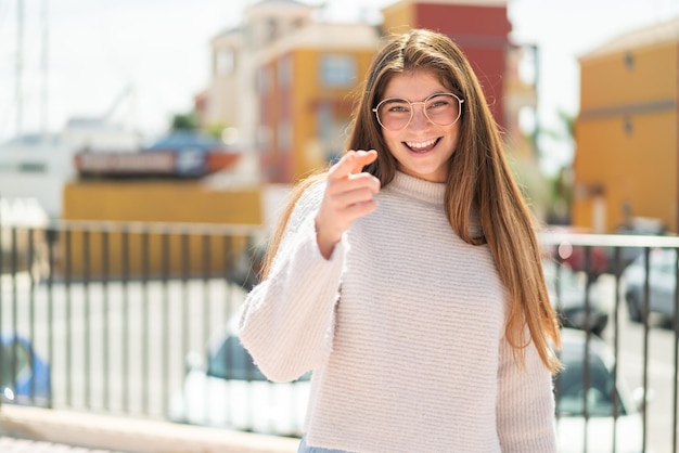 Foto giovane donna piuttosto caucasica con gli occhiali all'aperto sorpresa e che punta in avanti