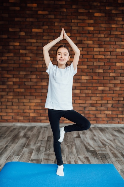 Young and pretty child in fitness clothes doing exercise at home.