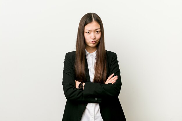 Young pretty chinese business woman frowning face in displeasure, keeps arms folded.