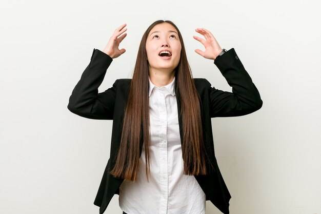 Young pretty chinese business woman screaming to the sky, looking up, frustrated.