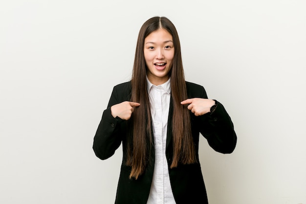 Young pretty chinese business woman surprised pointing with finger, smiling broadly