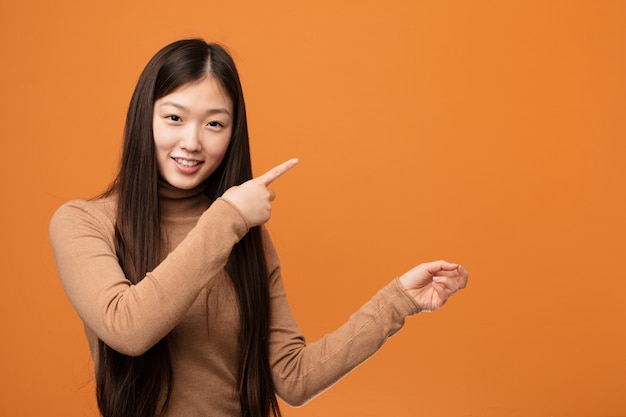 Молодая милая китайская женщина возбужденная указывая с указательными пальцами прочь.