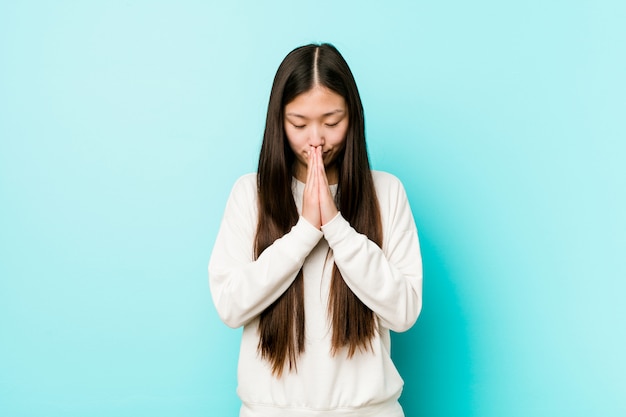 Young pretty chinese woman holding hands in pray near mouth, feels confident.