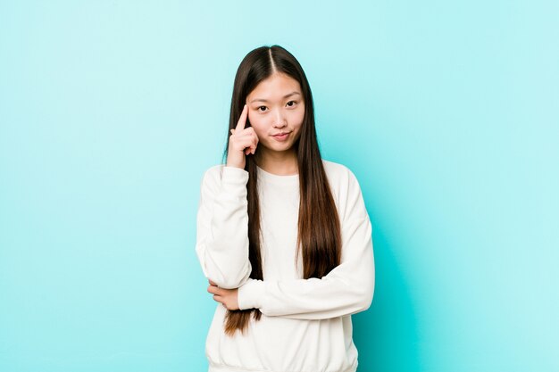 Young pretty chinese woman pointing temple with finger, thinking, focused on task.