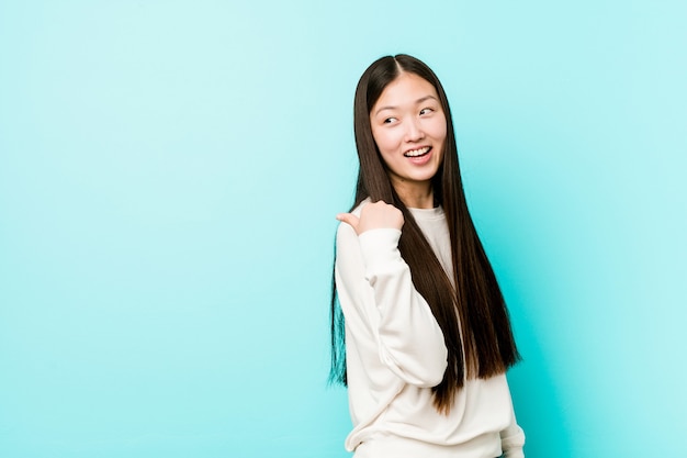 Young pretty chinese woman points with thumb finger away, laughing and carefree.