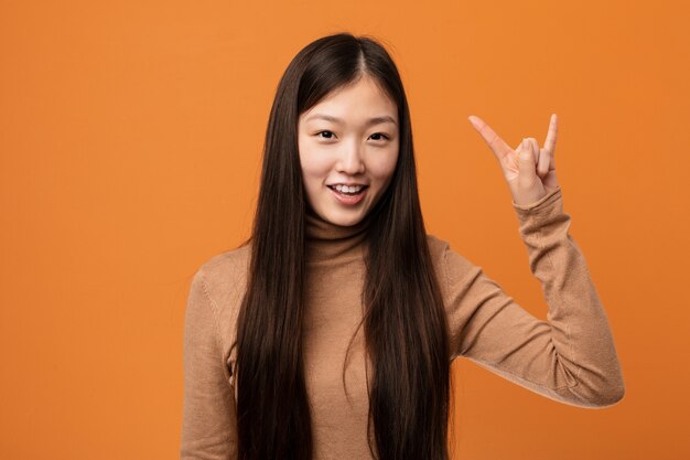 Young pretty chinese woman showing a horns gesture as a revolution concept.