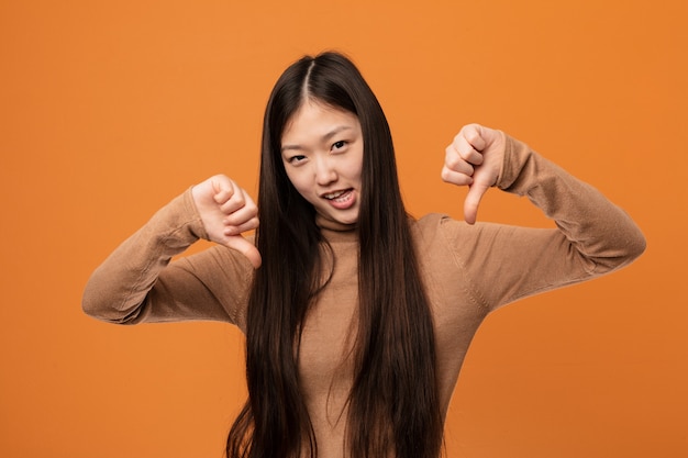 Young pretty chinese woman showing thumb down and expressing dislike.