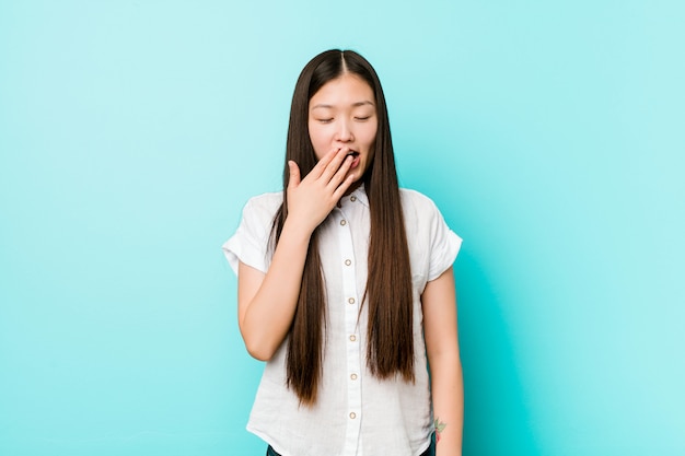 Young pretty chinese woman yawning showing a tired gesture covering mouth with hand.