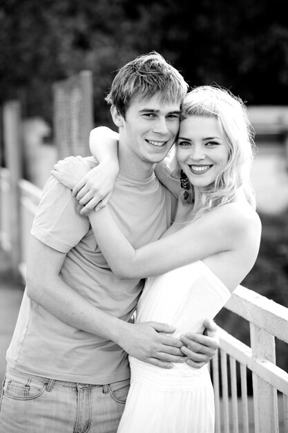 Young pretty couple charming girl in a white dress and a guy walks on the bridge on a warm summer sunny day