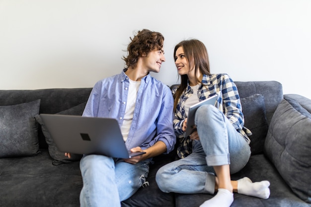 Young pretty couple relaxing on sofa with digital tablet and laptop.