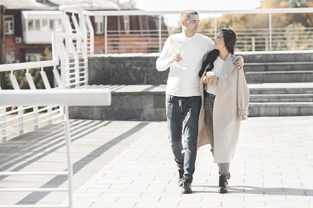 街の背景を歩いている若いかわいいカップル。都会の背景で一緒に楽しんでいる女性と男性。素敵な若者のデート。