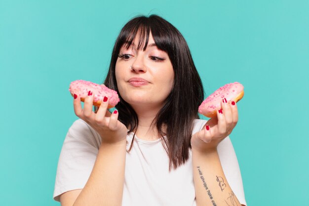 Young pretty curvy woman doubting or uncertain expression and holding a donut