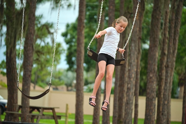 Молодая довольно взволнованная девочка-подросток прыгает с качелей в солнечный день летних каникул. Концепция опасности аварии