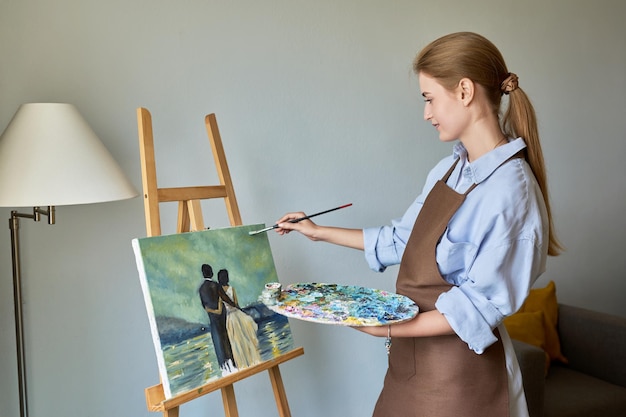 young pretty female artist painting with acrylics on an easel