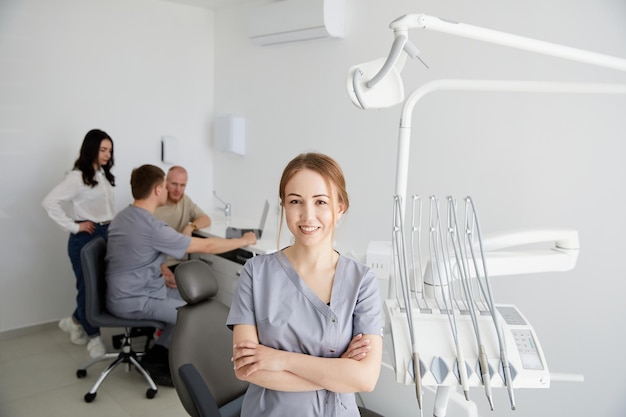 A young pretty female dentist stands in the middle of the office and in the background a colleague is advising patients Preparation for admission of patients