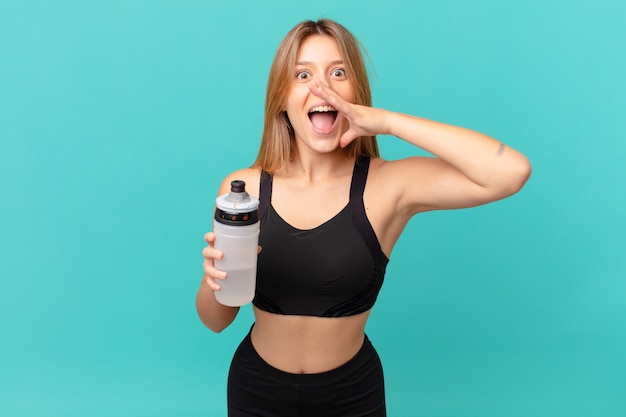 Young pretty fitness woman feeling happy,giving a big shout out with hands next to mouth