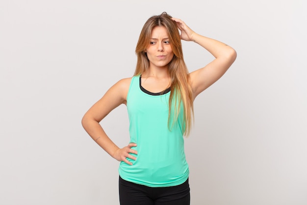 Young pretty fitness woman feeling puzzled and confused, scratching head