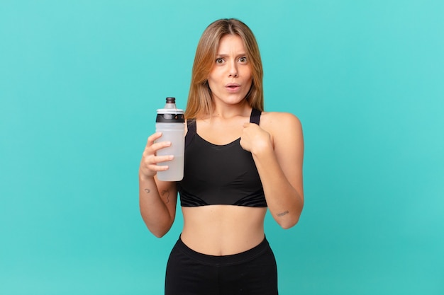 Young pretty fitness woman looking shocked and surprised with mouth wide open, pointing to self