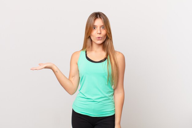 Young pretty fitness woman looking surprised and shocked, with jaw dropped holding an object