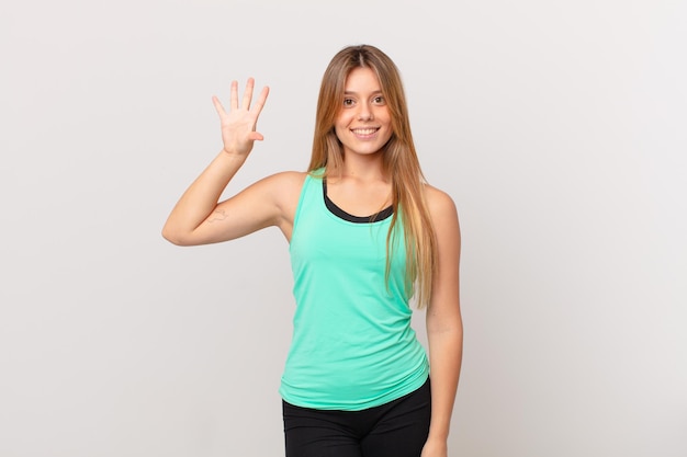 Young pretty fitness woman smiling and looking friendly, showing number five