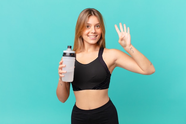 Young pretty fitness woman smiling and looking friendly, showing number four