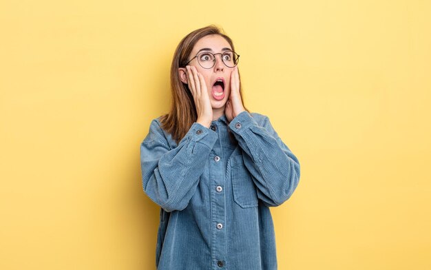 Young pretty girl feeling happy, excited and surprised, looking to the side with both hands on face