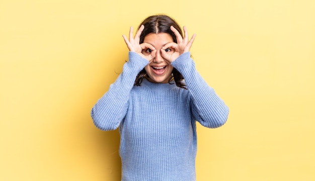young pretty girl feeling shocked, amazed and surprised, holding glasses with astonished, disbelieving look