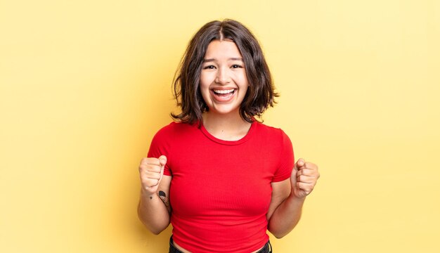 Young pretty girl feeling shocked, excited and happy, laughing and celebrating success, saying wow!