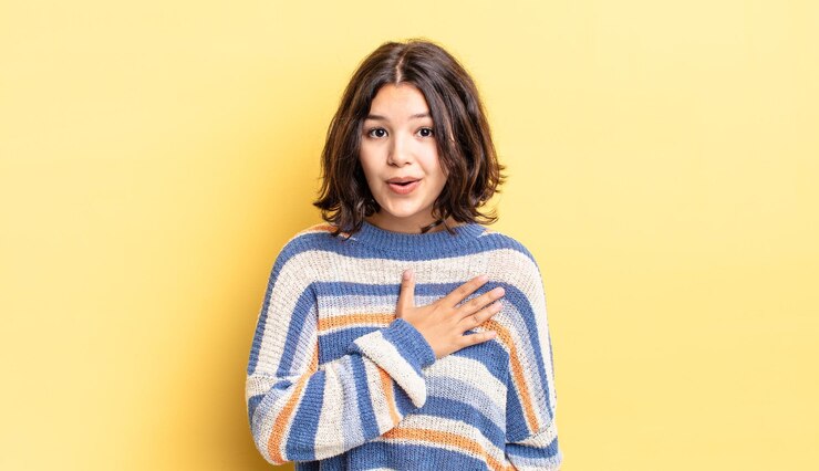 Photo ショックを受けて驚いた若いかわいい女の子は、笑顔で、心に手を取り合って、一人になって幸せであるか、感謝の気持ちを示しています