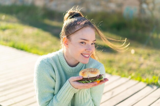 Photo young pretty girl holding a burger at outdoors