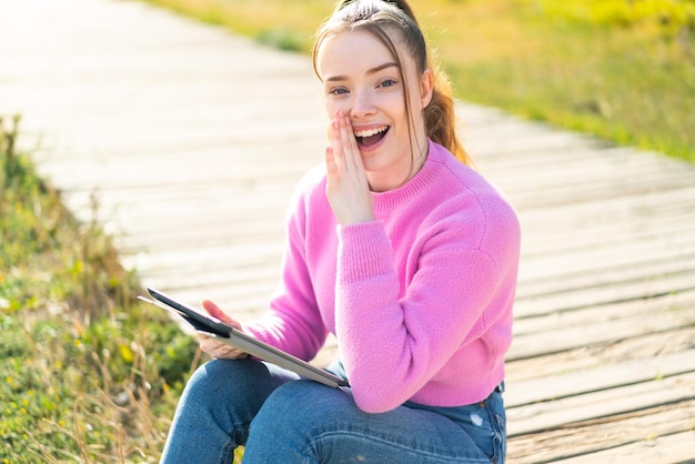 Young pretty girl holding a tablet at outdoors whispering something