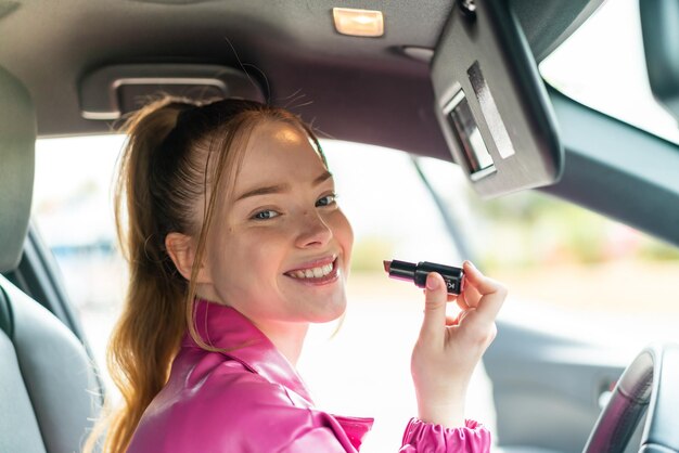 赤い口紅を保持している車の中の若いきれいな女の子