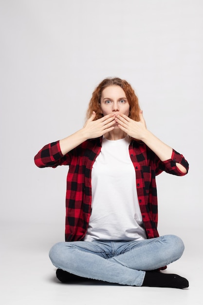 A young pretty girl is sitting on a white background in a plaid shirt