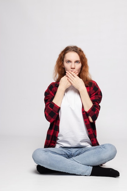 A young pretty girl is sitting on a white background in a plaid shirt