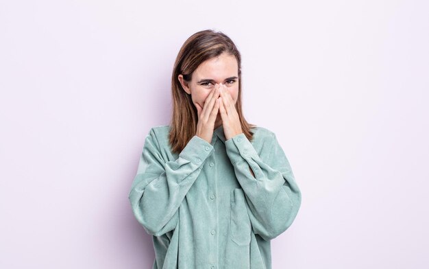 Young pretty girl looking happy, cheerful, lucky and surprised covering mouth with both hands