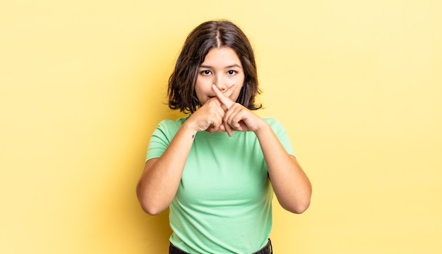 Young pretty girl looking serious and displeased with both fingers crossed up front in rejection, asking for silence