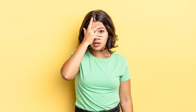 Young pretty girl looking shocked, scared or terrified, covering face with hand and peeking between fingers