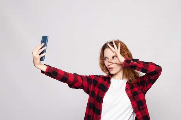 Photo young pretty girl makes a selfie photo in the studio on a light background