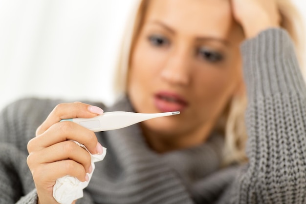 A young pretty girl, out of focus, worriedly looking at a digital thermometer that is in the foreground.