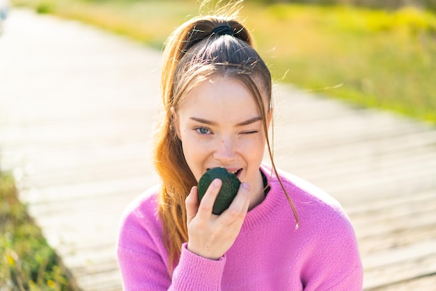 Giovane ragazza graziosa all'aperto che tiene un avocado