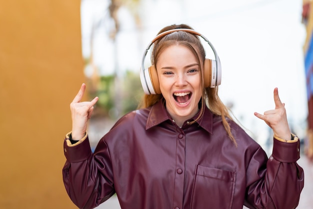ロック ジェスチャーを作る音楽を聴く屋外で若いきれいな女の子