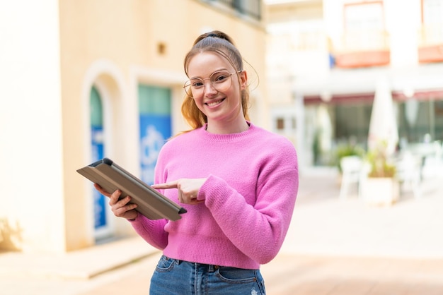 Young pretty girl at outdoors touching the tablet screen with happy expression