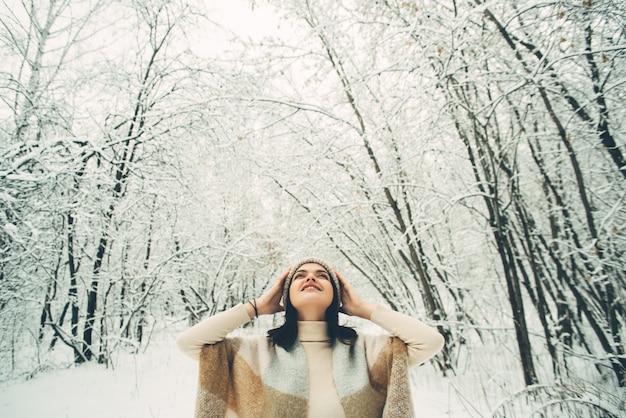 見上げる雪に覆われた森の格子縞の下で若いきれいな女の子。冬の気分。