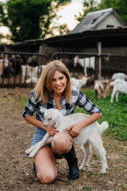 A young pretty girl poses on a ranch with goats and other animals. Agriculture, livestock breeding.