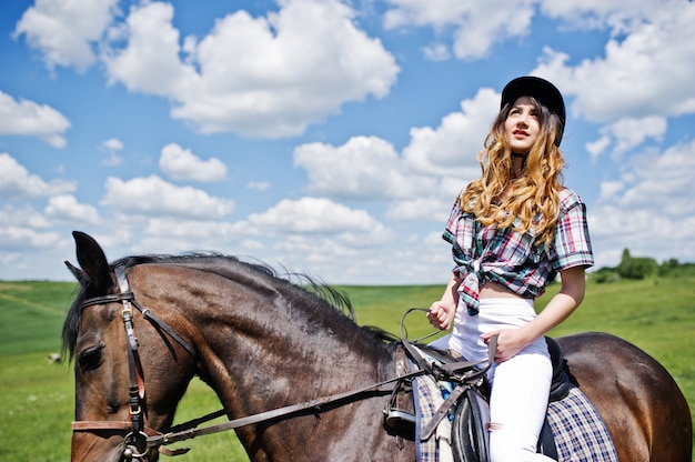 Young pretty girl riding a horse on a field at sunny day.