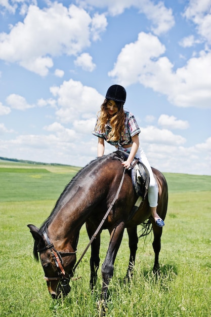 Young pretty girl riding a horse on a field at sunny day